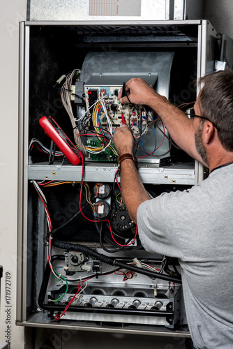 Mechanic works on a home furnace with volt meter