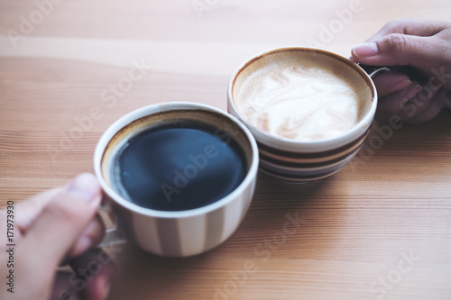 Top view image of man and woman's hands holding coffee cups with wooden table background