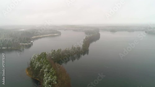 Flying and rising over lake with narrow treeline forest covered with light snow during spring snowy misty day, Liesjarvi, Finland photo