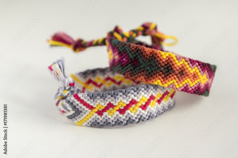 Fototapeta premium Two simple handmade homemade natural woven bracelets of friendship on white background, rainbow colors, checkered pattern
