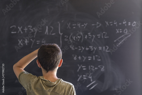 Schoolboy solving a problem on a blackboard.
