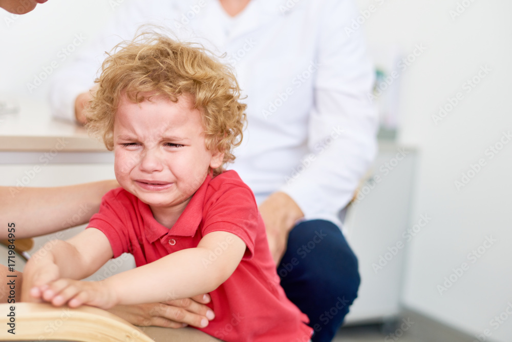 Portrait of curly little patient crying hysterically at pediatrician office refusing to be examined, blurred background Portrait of curly little patient crying hysterically at pediatrician office refusing to be examined, blurred background