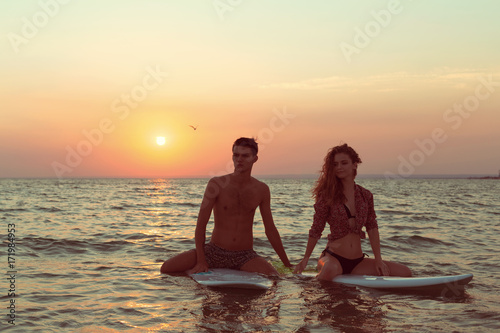 Surfing couple leaning on surfboards in sea