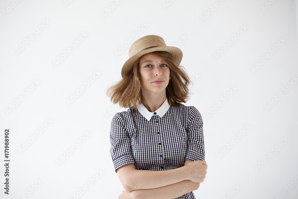 People, style and fashion concept. Isolated picture of attractive joyful young woman wearing summer straw hat and retro dress posing in studio with arms folded, her hair streaming in the air People, style and fashion concept. Isolated picture of attractive joyful young woman wearing summer straw hat and retro dress posing in studio with arms folded, her hair streaming in the air