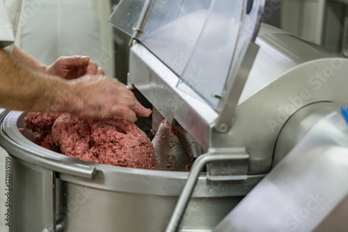 Butcher grounding meat in grinder machine to make sausages