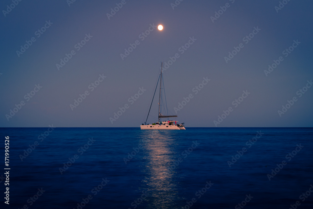 Full moon over the pinarello bay with cool reflection on the sea and a sailing ship.