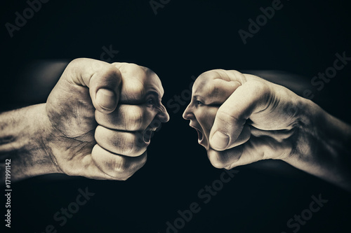 Two fists with a male and female face collide with each other on black background. Concept of confrontation, competition, family quarrel etc. photo