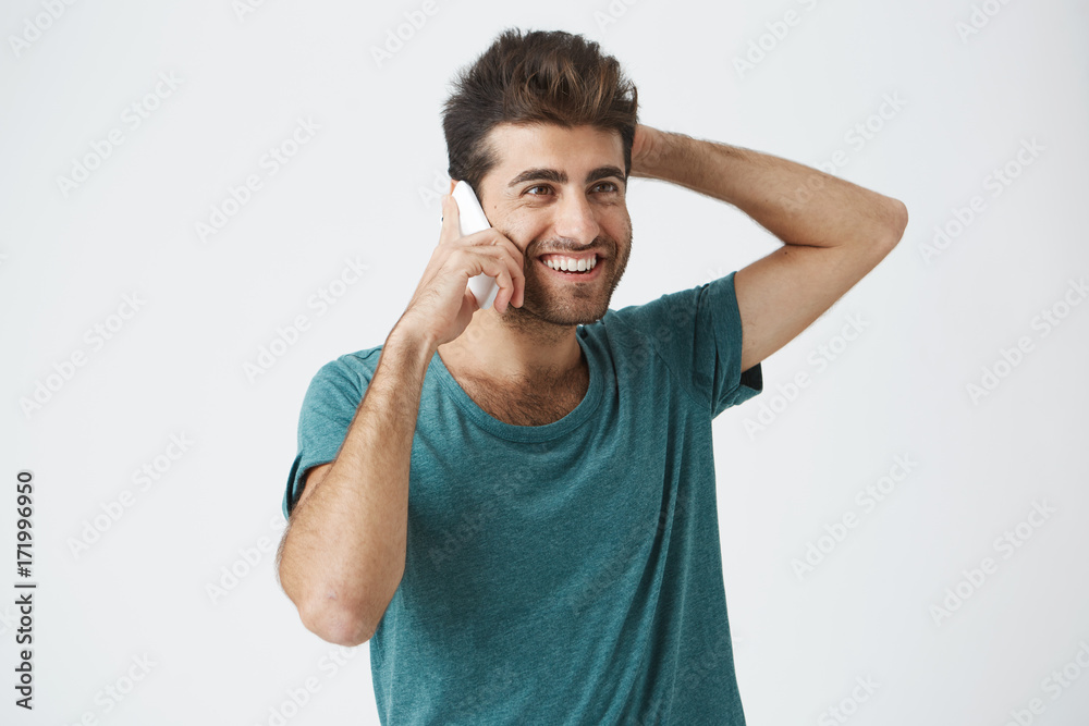 Close up isolated portrait of smiling spanish male in trendy t-shirt, smiling and holding his head, while talking on the phone with best friend. Close up isolated portrait of smiling spanish male in trendy t-shirt, smiling and holding his head, while talking on the phone with best friend.