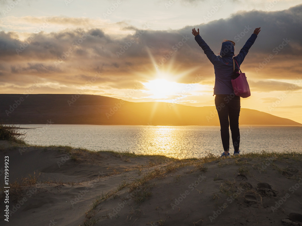 Sunset over Atlantic ocean, West coast of Ireland, a woman with her hands high, showing excitement.