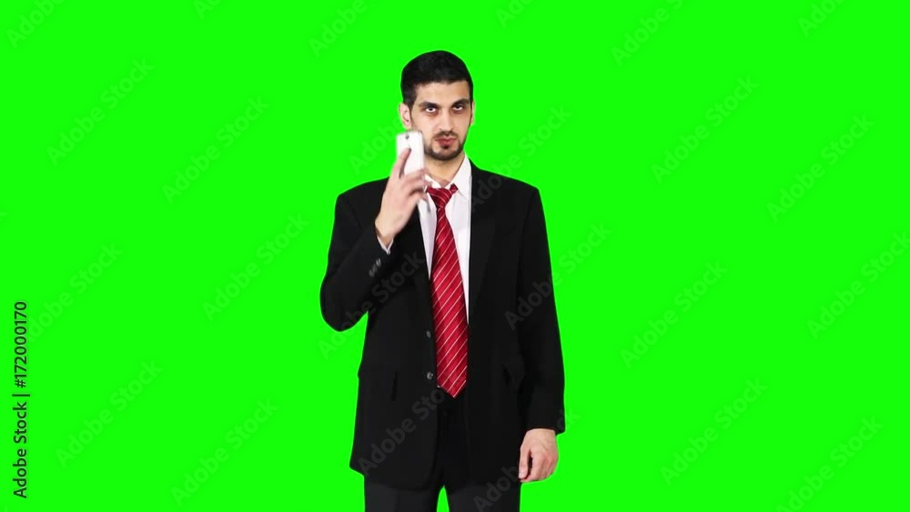 Young Caucasian businessman speaking on a smartphone while wearing formal suit and standing in front of green screen background at studio Young Caucasian businessman speaking on a smartphone while wearing formal suit and standing in front of green screen background at studio