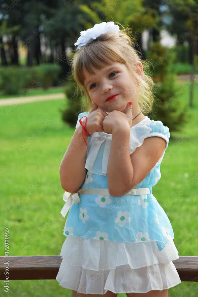 little girl with blond hair with a white bow in a blue dress playing in the park little girl with blond hair with a white bow in a blue dress playing in the park