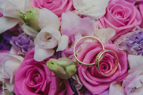 Golden wedding rings on flowers bouqet made of white and pink roses.