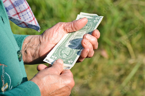 The old woman is holding money in her hands. An elderly woman with dollars in her hands. Poverty alms
