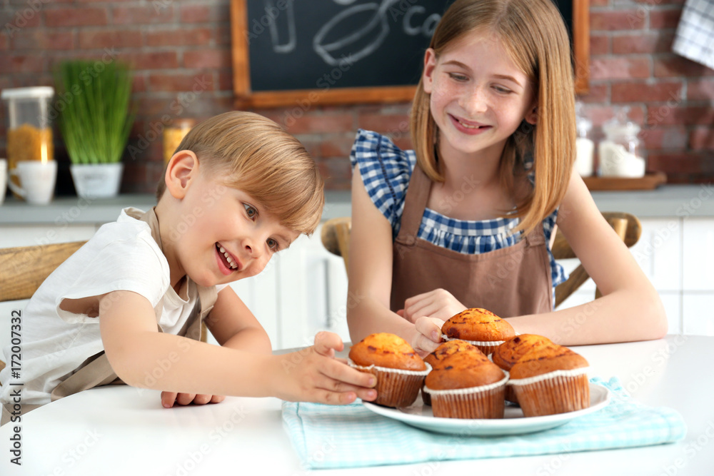 Boy and girl eating yummy muffins in kitchen. Cooking classes concept