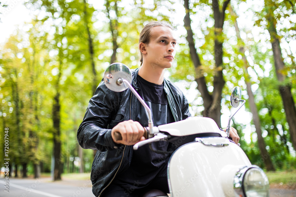 Obraz premium fashionable young man riding a vintage scooter in the street