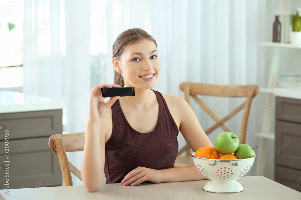 Beautiful young woman with energy bar sitting at table. Diet concept