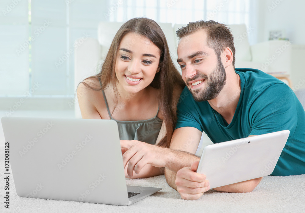Young couple searching information using laptop and tablet at home