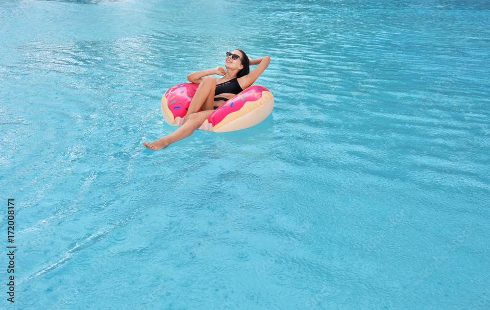 Beautiful young woman on inflatable donut in swimming pool