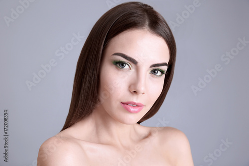 Young beautiful woman with fancy green makeup on grey background