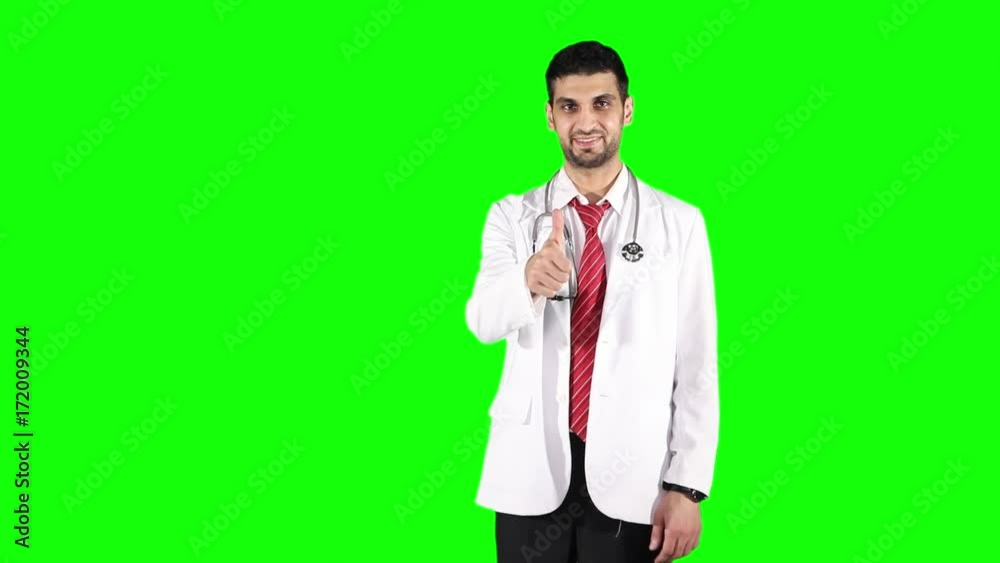 Male Caucasian physician pointing at copy space and showing thumb up while smiling and standing against green screen background Male Caucasian physician pointing at copy space and showing thumb up while smiling and standing against green screen background