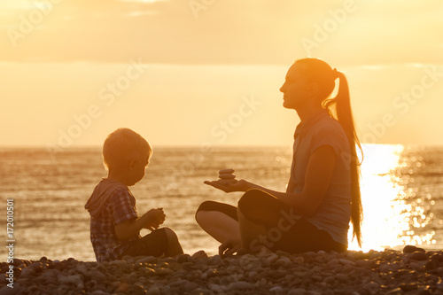 Mom and son playing on the beach with stones. Sunset time, silhouettes