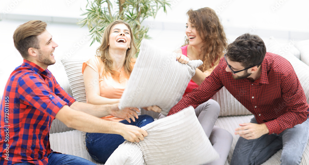 cheerful friends playing with the pillows sitting on the couch