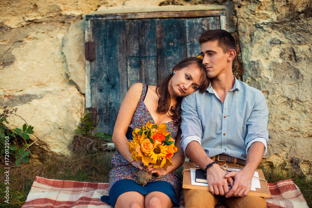 Φωτογραφία Sensual lovely couple sitting on the plaid near the rock with caves and blue wooden door