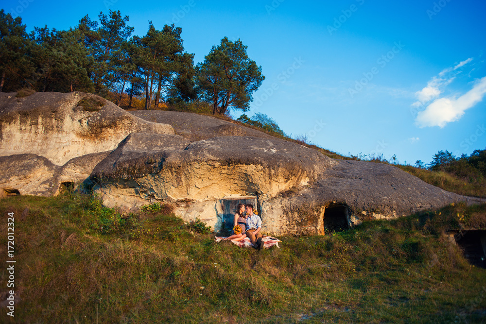 Φωτογραφία Sensual lovely couple sitting on the plaid near the rock with caves and blue wooden door