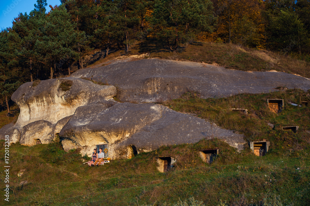 Φωτογραφία Sensual lovely couple sitting on the plaid near the rock with caves and blue wooden door