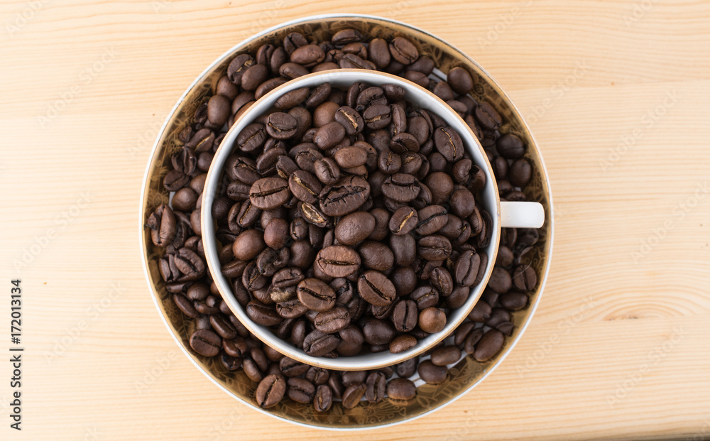 Cup and saucer filled with coffee beans on wooden table view from above Cup and saucer filled with coffee beans on wooden table view from above