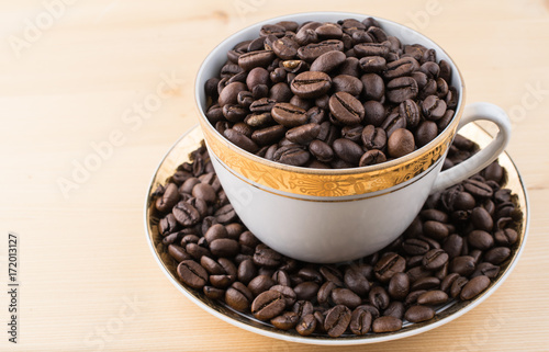 Cup and saucer filled with coffee beans on wooden table