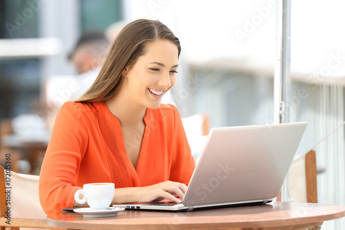 Lady in orange typing in a laptop in a restaurant