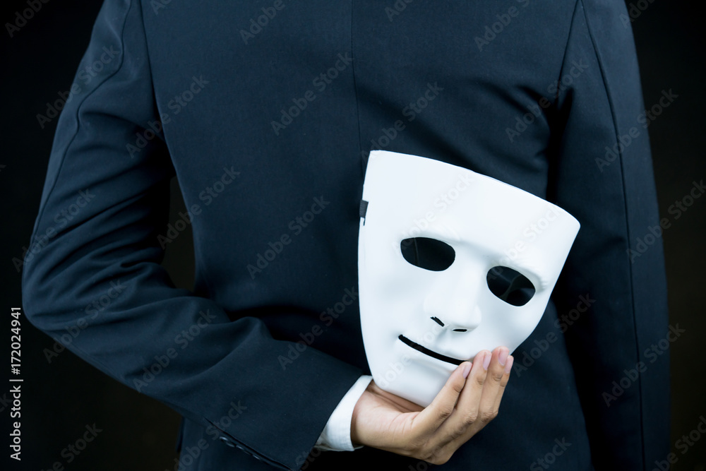 businessman hide the white mask in the hand behind his back on black  background. Stock Photo | Adobe Stock