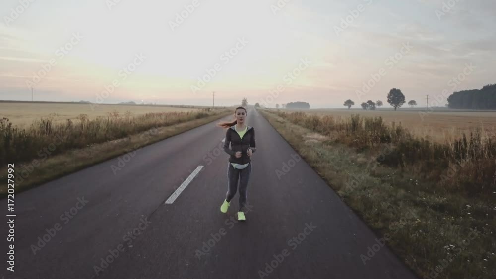 AERIAL 4K: Woman Running on a Countryside Road at Sunrise. Drone shot of a Female jogger athlete training at dusk. Active healthy lifestyle concept. Cinematic morning sports footage. AERIAL 4K: Woman Running on a Countryside Road at Sunrise. Drone shot of a Female jogger athlete training at dusk. Active healthy lifestyle concept. Cinematic morning sports footage.