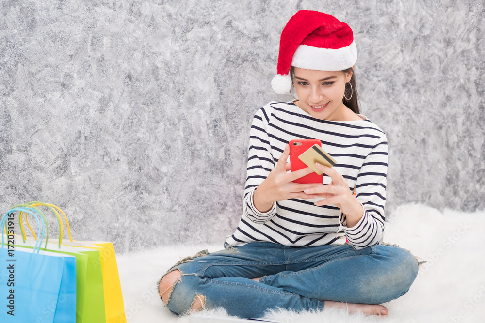 Obraz premium Beautiful young girl wearing a Santa hat holding lots of shopping bags in the festive season