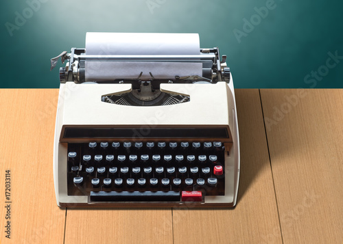 Old vintage typewriter with white blank paper on wooden brown table