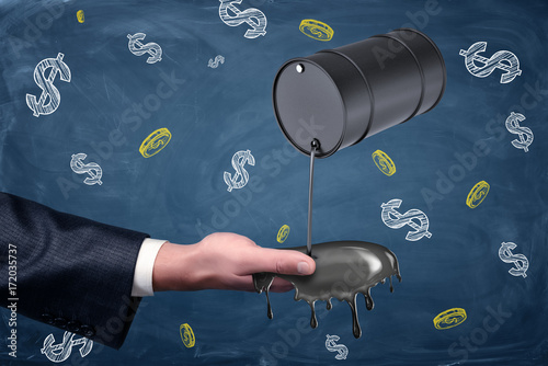 A businessman's hand reaching out to catch oil leaking from a small black barrel. photo