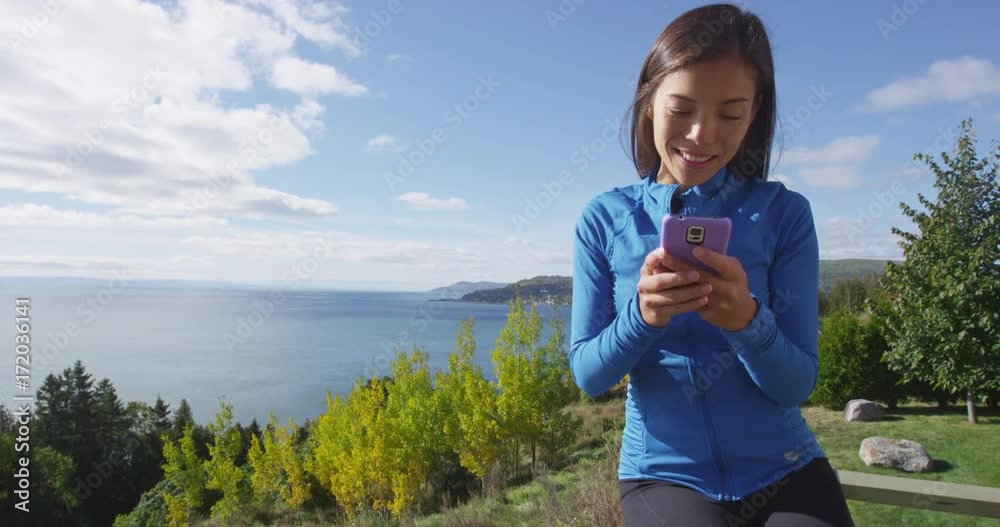 Woman using phone app in autumn fall nature - smartphone concept. Girl using cellphone in sporty running fitness clothing by sea and mountain forest landscape. RED EPIC SLOW MOTION,
