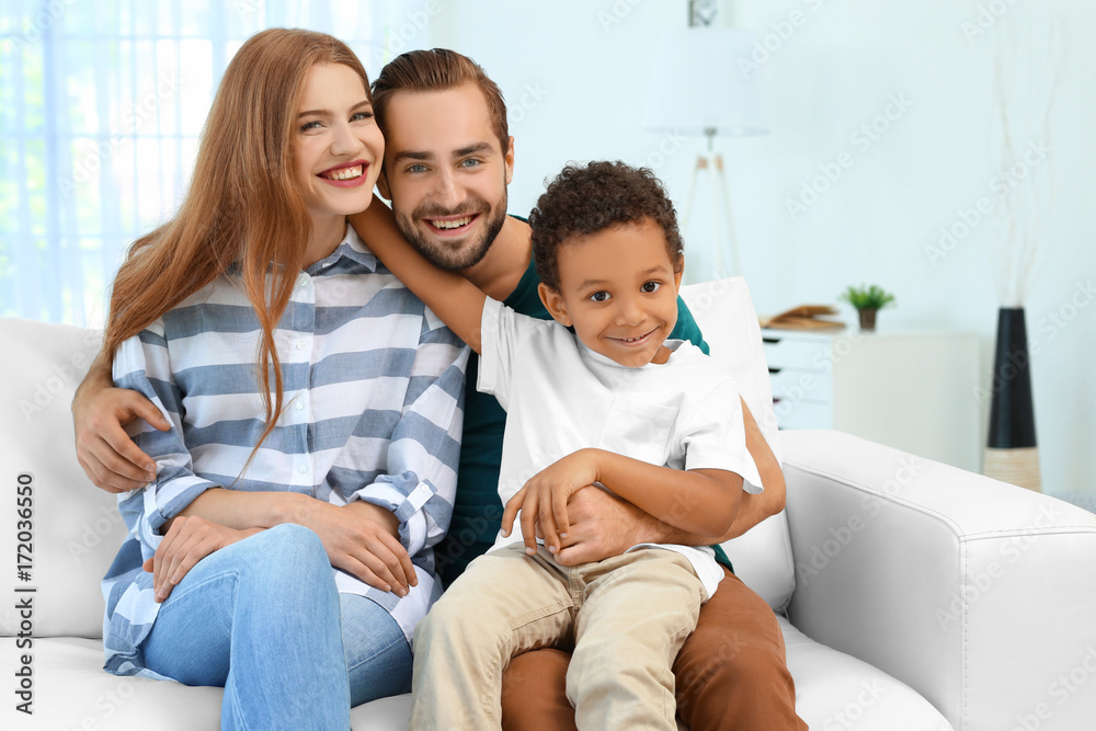 Happy couple with adopted African-American boy sitting on couch at home Happy couple with adopted African-American boy sitting on couch at home