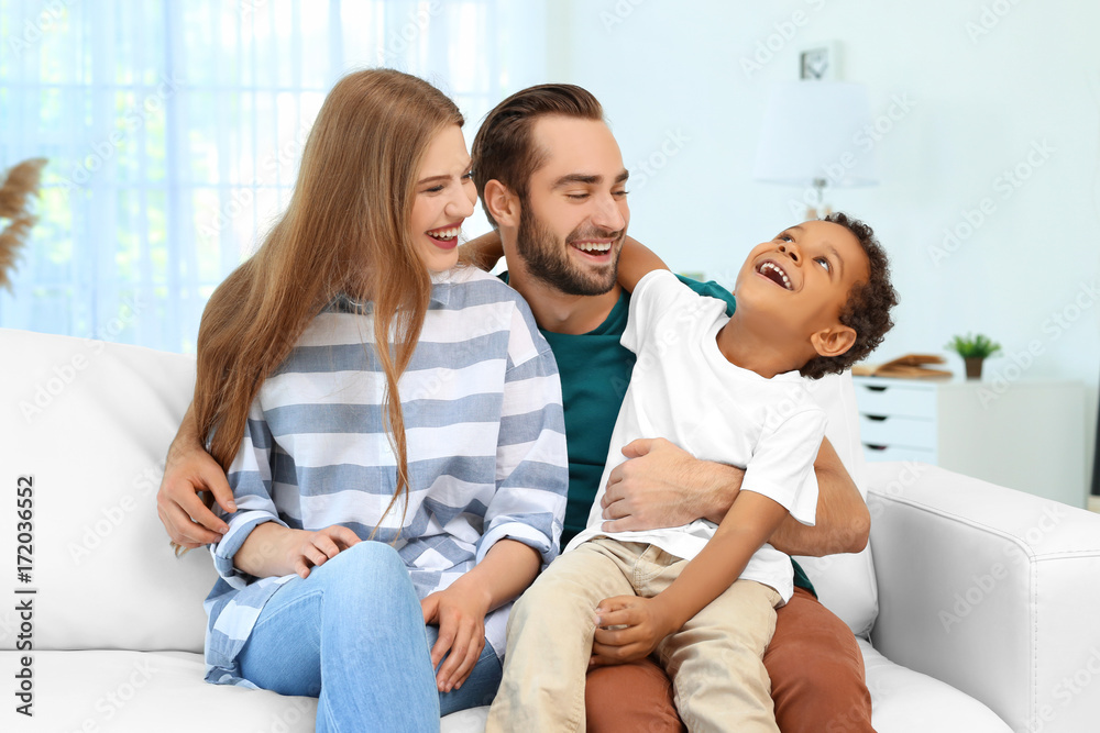 Happy couple with adopted African-American boy sitting on couch at home Happy couple with adopted African-American boy sitting on couch at home