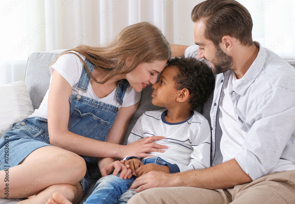 Fototapeta premium Happy couple with adopted African-American boy sitting on couch at home