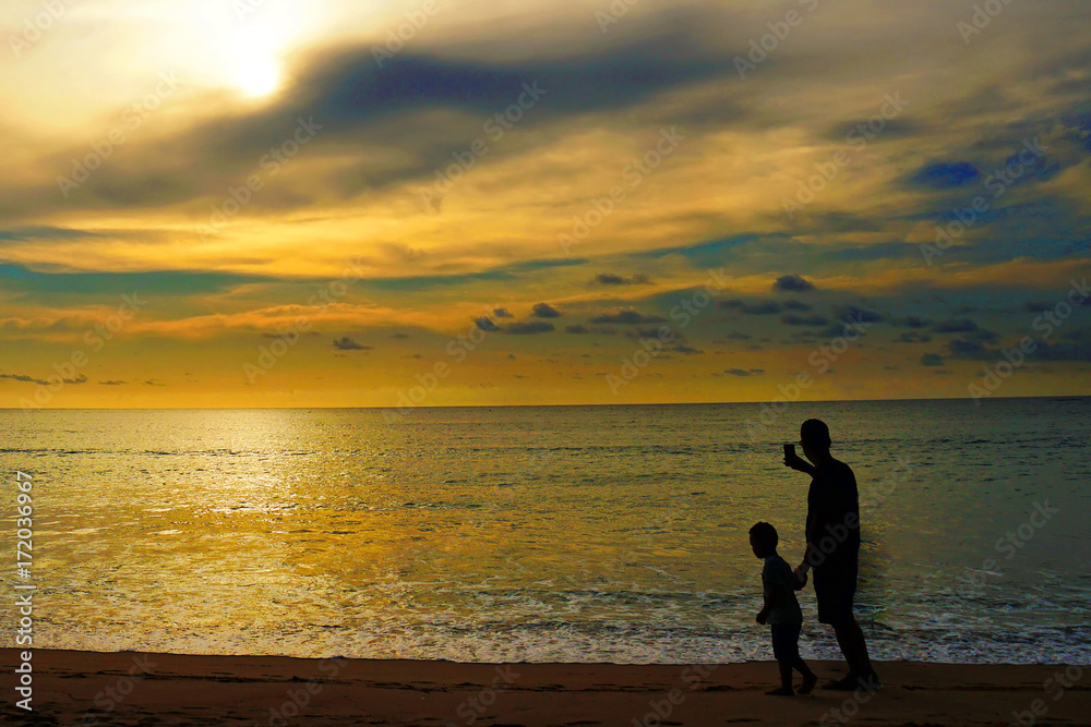 Silhouette of Dad and kid over sunset on summer ocean