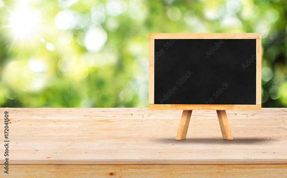 Blackboard menu with easel on wooden table top (food stand) with blur  garden green nature bokeh and leaf at foreground,Mock up for display or  montage of product or design Stock Photo