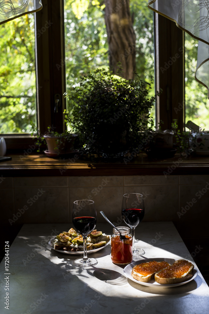 two glasses of red wine with sandwiches with red caviar and bruschettes with cheese and figs. in the kitchen at the window