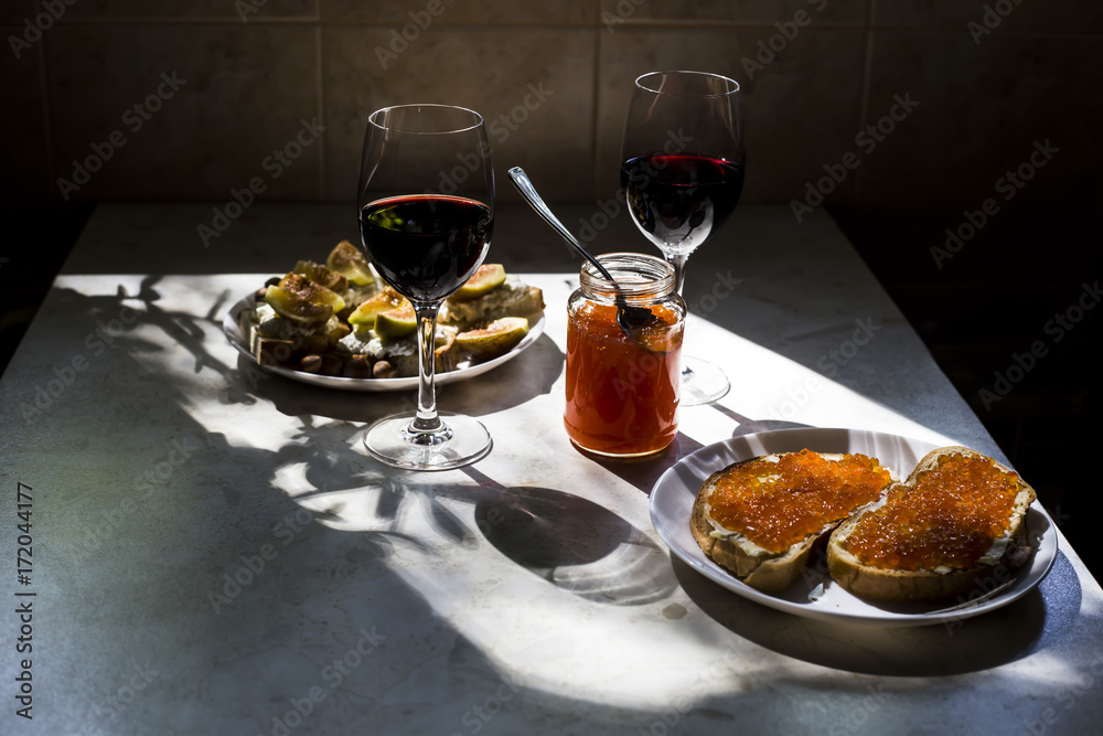 two glasses of red wine with sandwiches with red caviar and bruschettes with cheese and figs. in the kitchen at the window