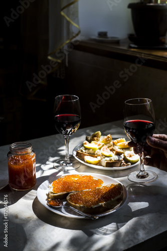 two glasses of red wine with sandwiches with red caviar and bruschettes with cheese and figs. in the kitchen at the window