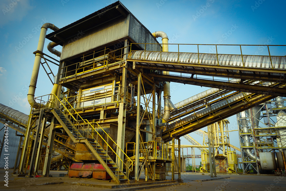 Particle board factory view of conveyor, lighting pole, building, logs storage Particle board factory view of conveyor, lighting pole, building, logs storage