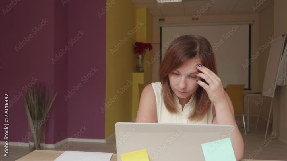 Disappointed girl sits in front of laptop, writes and throw paper about