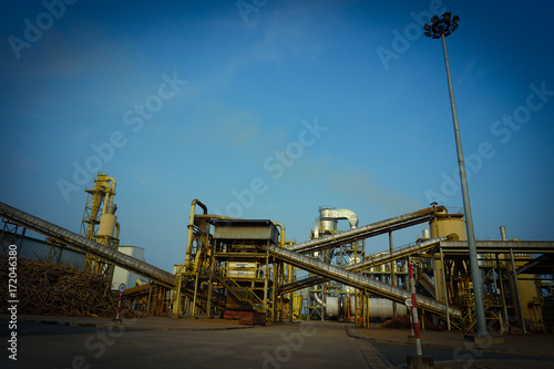 Particle board factory view of conveyor, lighting pole, building, logs storage