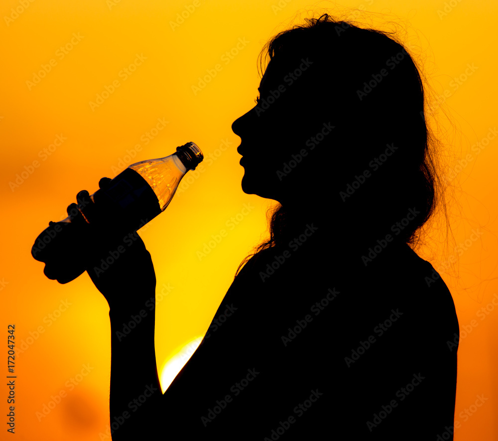Silhouette of a girl drinking water at sunset